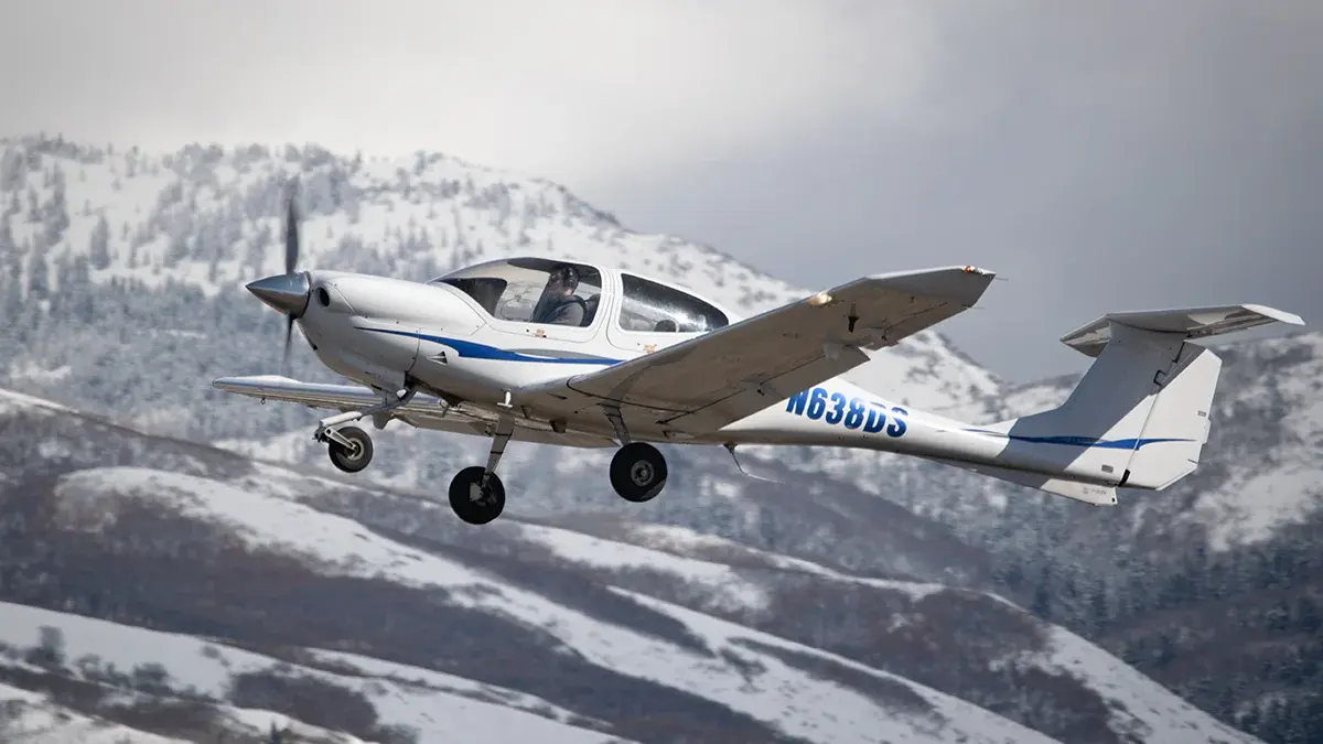 A small aircraft in flight with snowy mountains in the background.